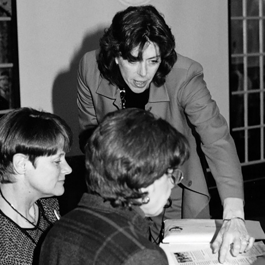 Woman in blazer points to document with two women looking on