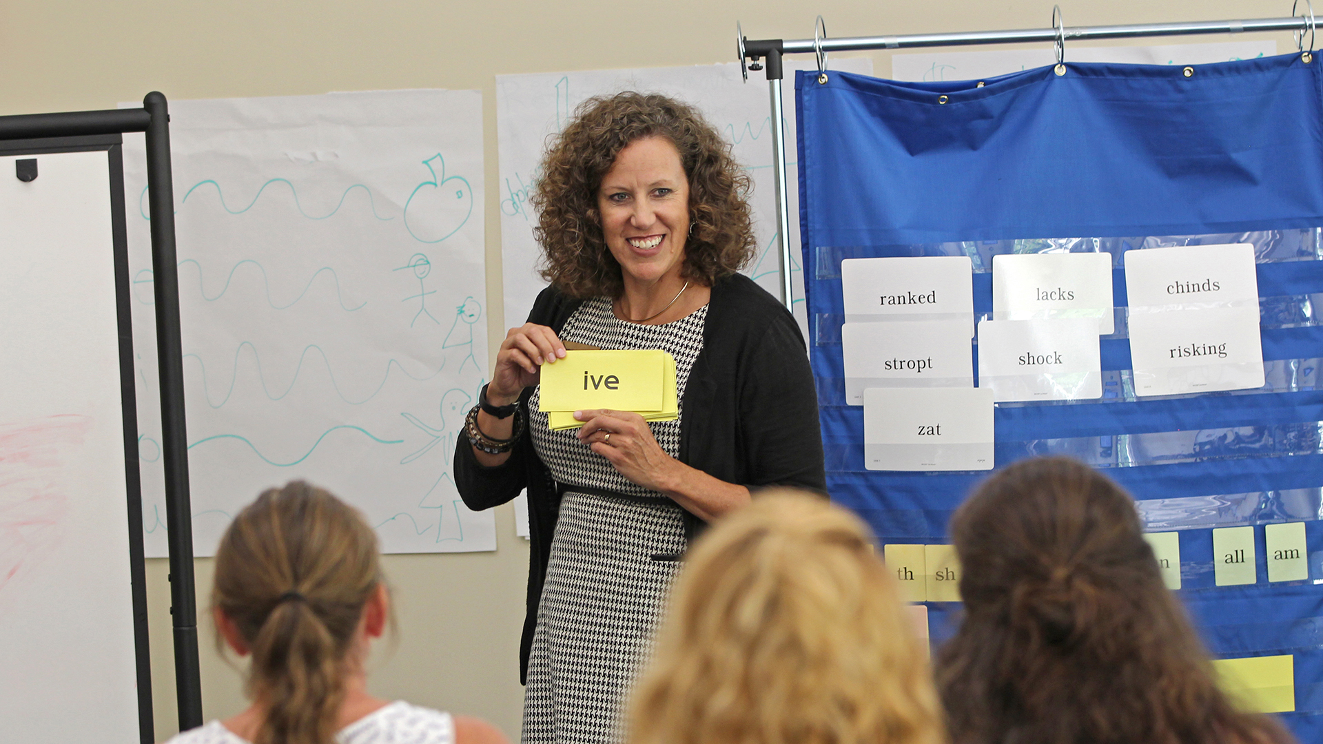 Teacher holds "ive" card, teaching reading to students in classroom