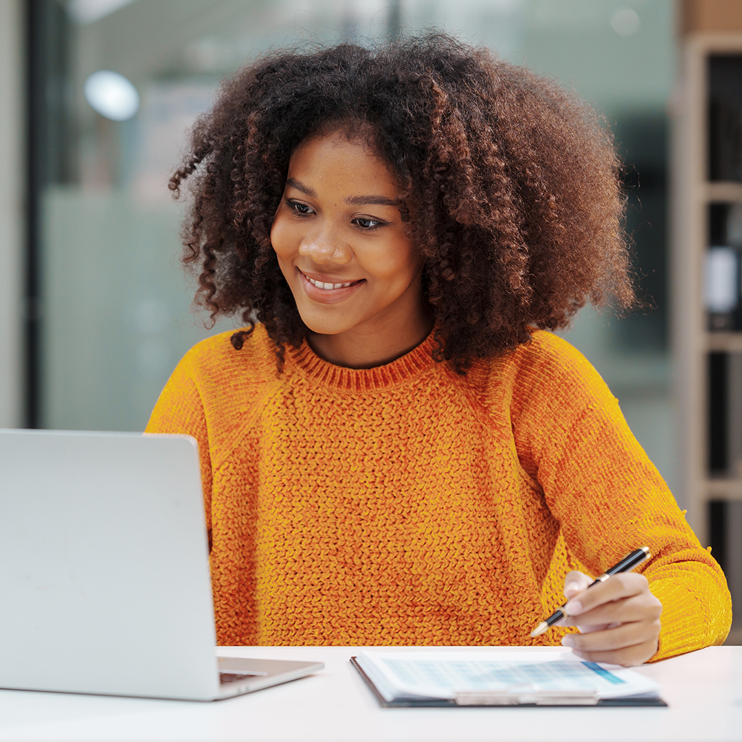 Young woman smiling while studying online on her laptop, part of an online learning community.