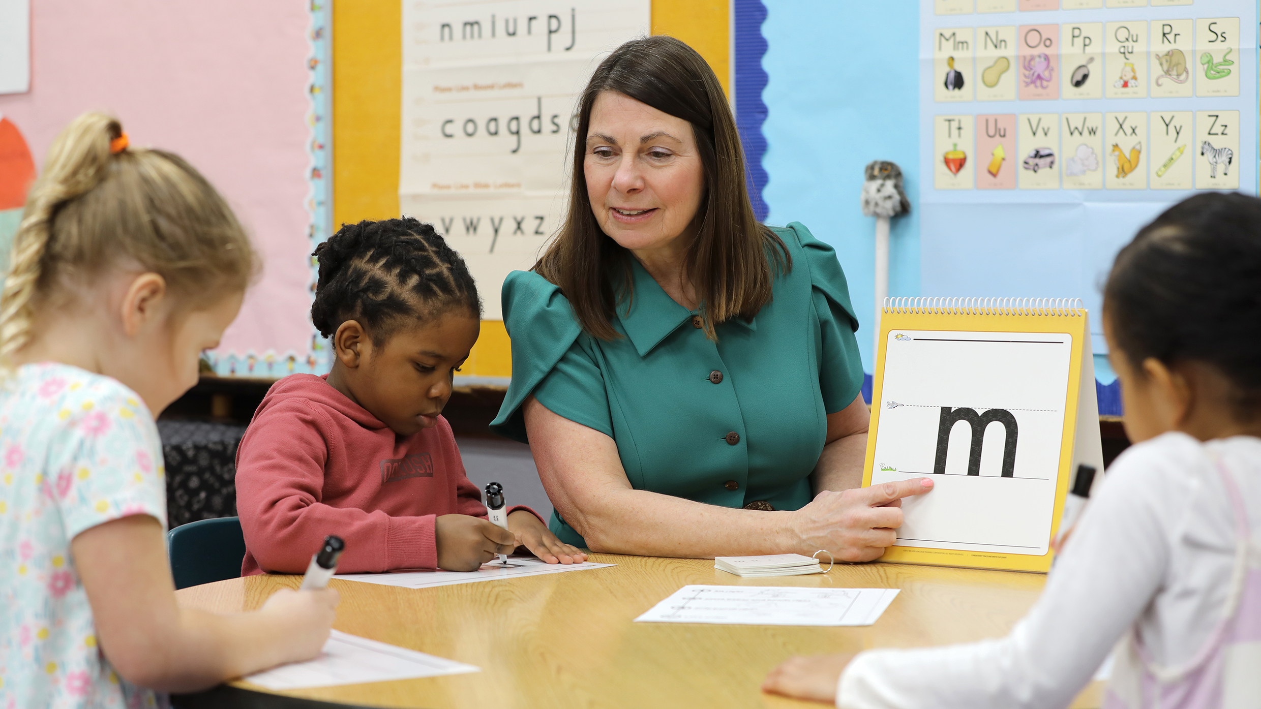 Teacher points to letter 'm' on flashcard with young students in Pre-K activity