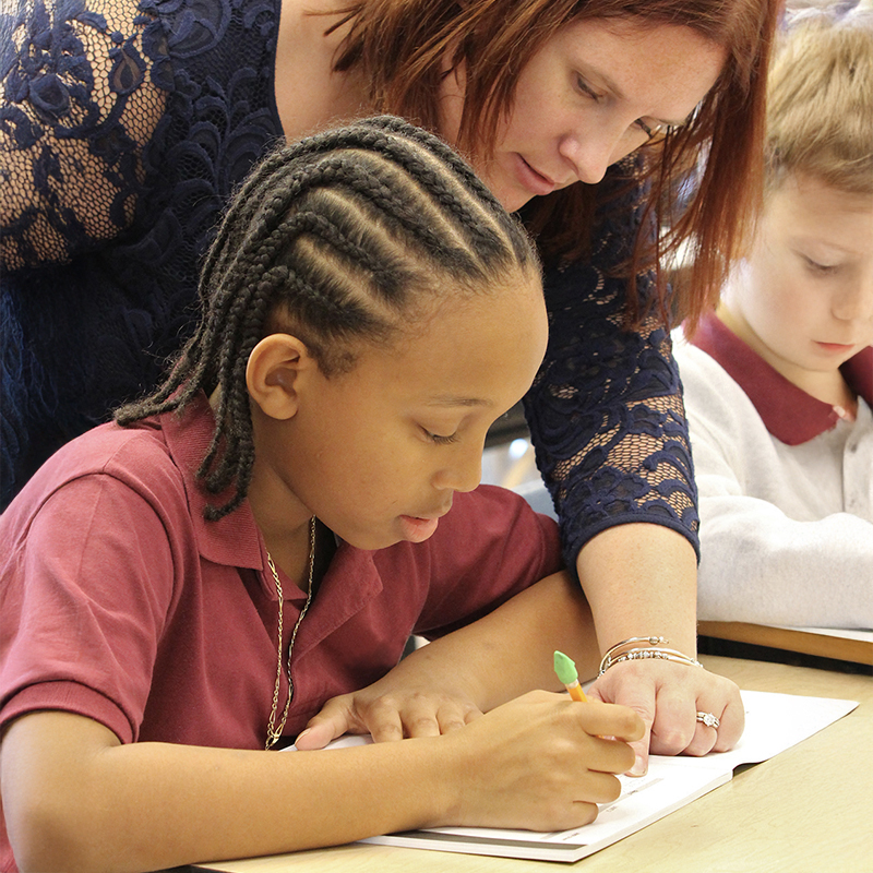 Teacher helps student with writing assignment in classroom, Just Words®