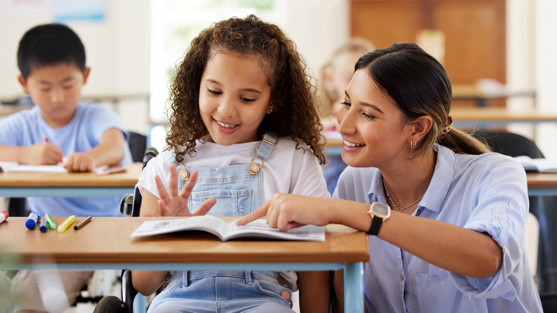Teacher helps a young girl in a wheelchair with Fundations K-3 reading.