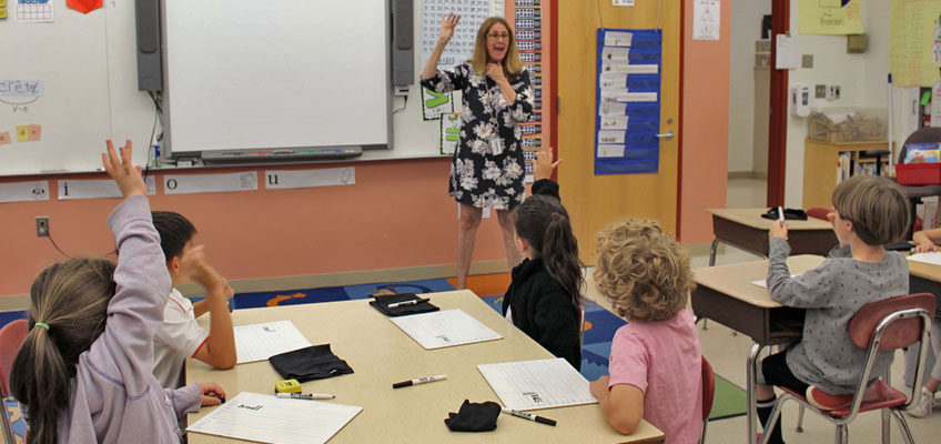 Teacher leading Fundations lesson with engaged students raising hands