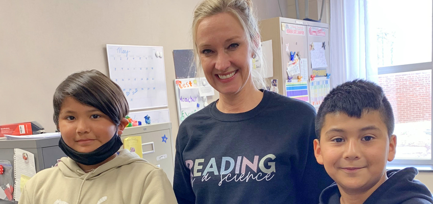 Teacher with two fourth graders, one wearing a mask, celebrating success with Wilson Reading System.