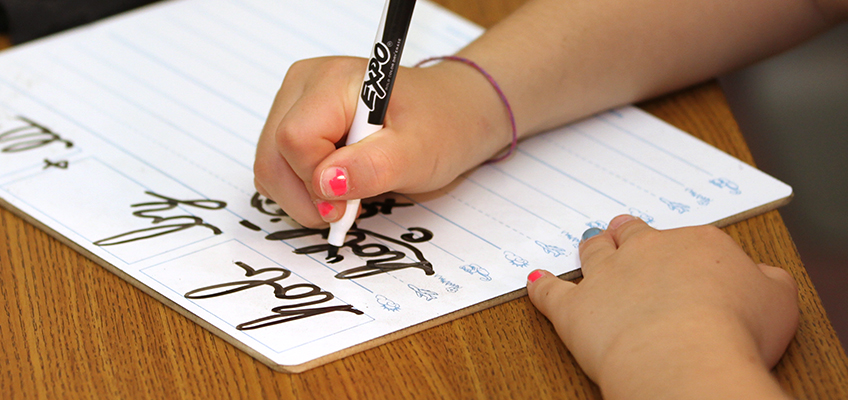 Child practicing cursive writing on a whiteboard, learning 