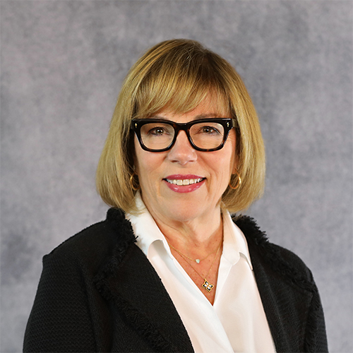 Portrait of a woman with blonde hair, glasses, and a black jacket.
