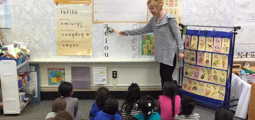 Teacher pointing to alphabet chart with young students watching