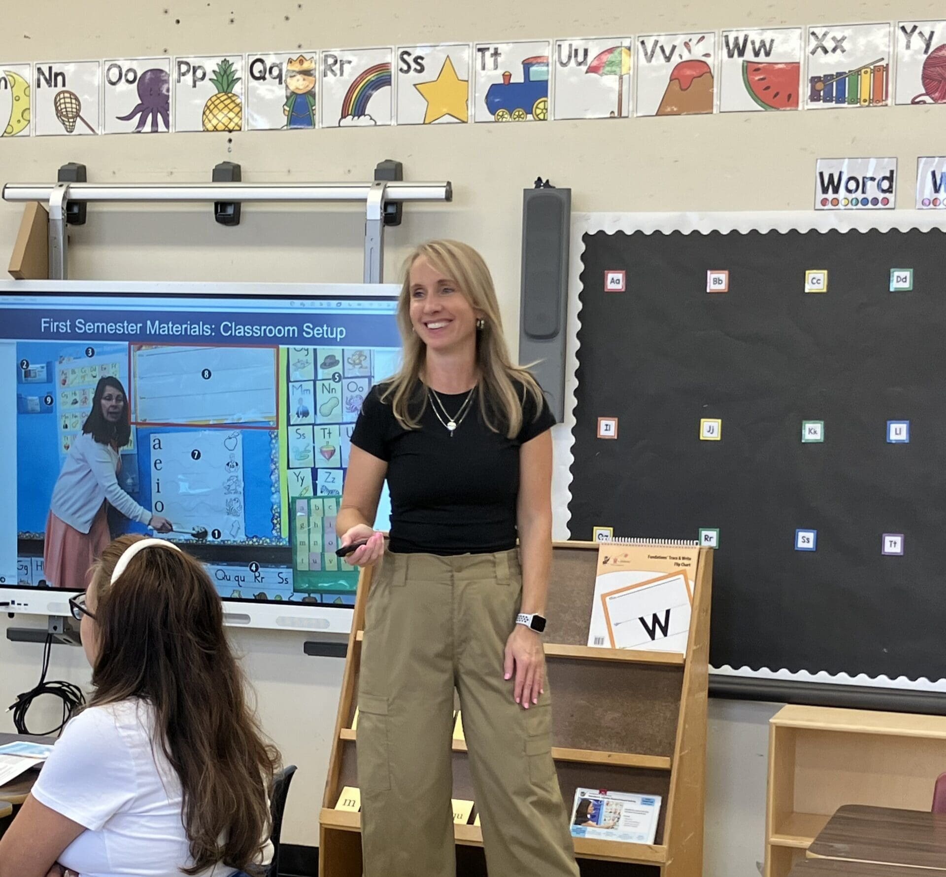 Literacy specialist in a classroom, pointing to a screen with alphabet letters.