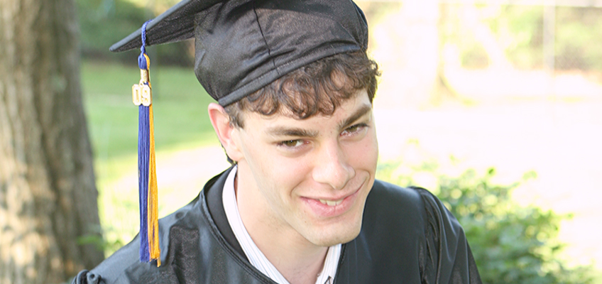 Young man in graduation cap and gown, smiling, symbolizing overcoming adversity