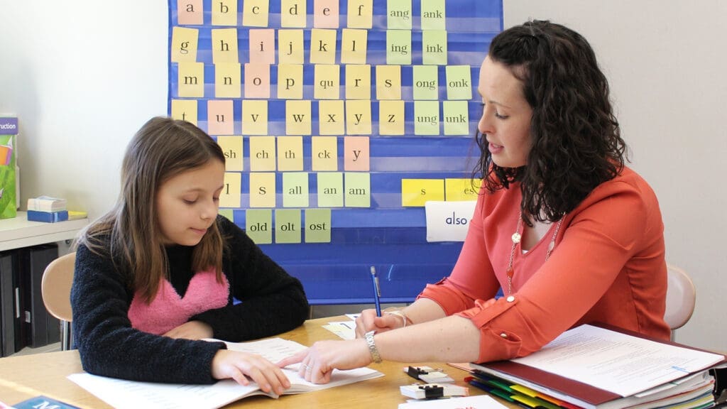 Teacher and student learning phonics with letter cards for dyslexia training.