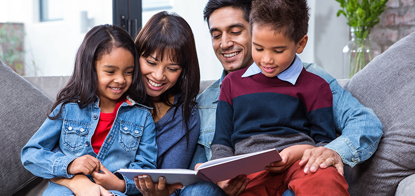 Family reading a book together, promoting student learning and family literacy.